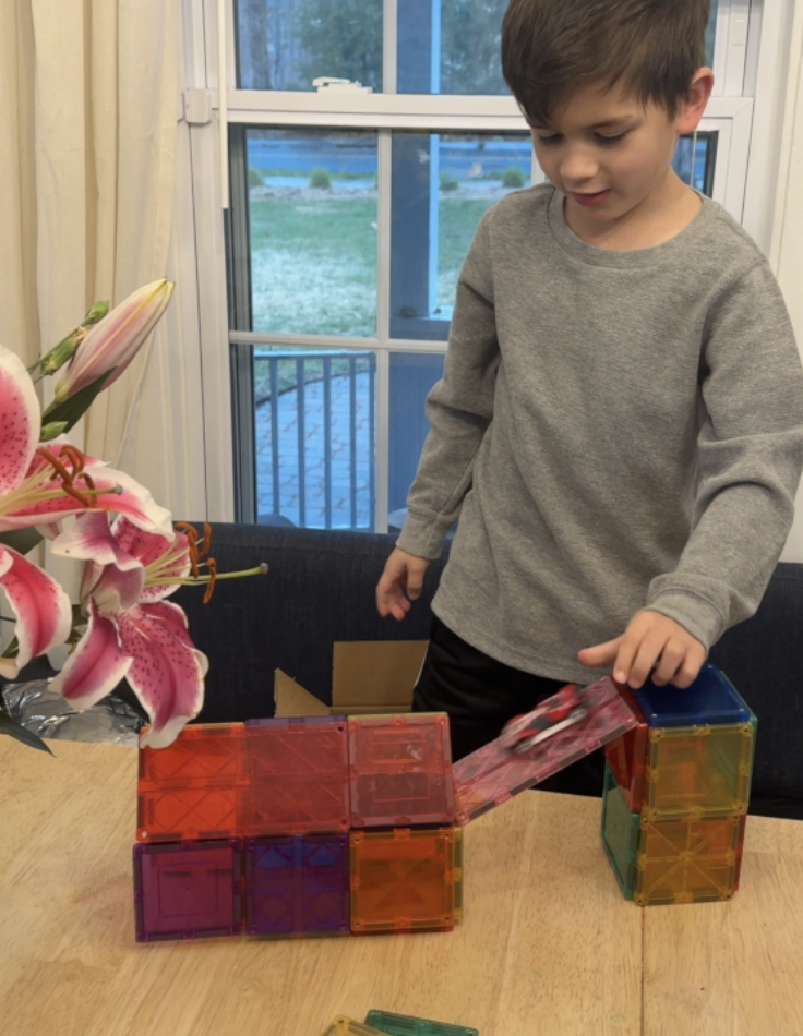 Boy playing with magnet tiles on table with toy car.