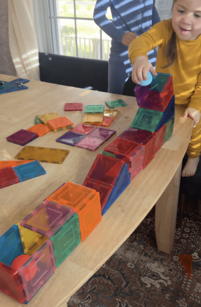 Girl playing with magnet tiles and ball on table.